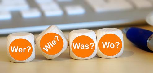 Holzwürfel mit orange-farbendem Kreis und Fragen Holzwürfel mit orange-farbendem Kreis und W-Fragen